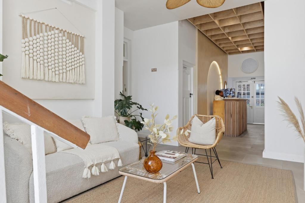 Bright modern living area with white walls, beige sofa, and woven chairs arranged around a glass coffee table on a natural fiber rug.