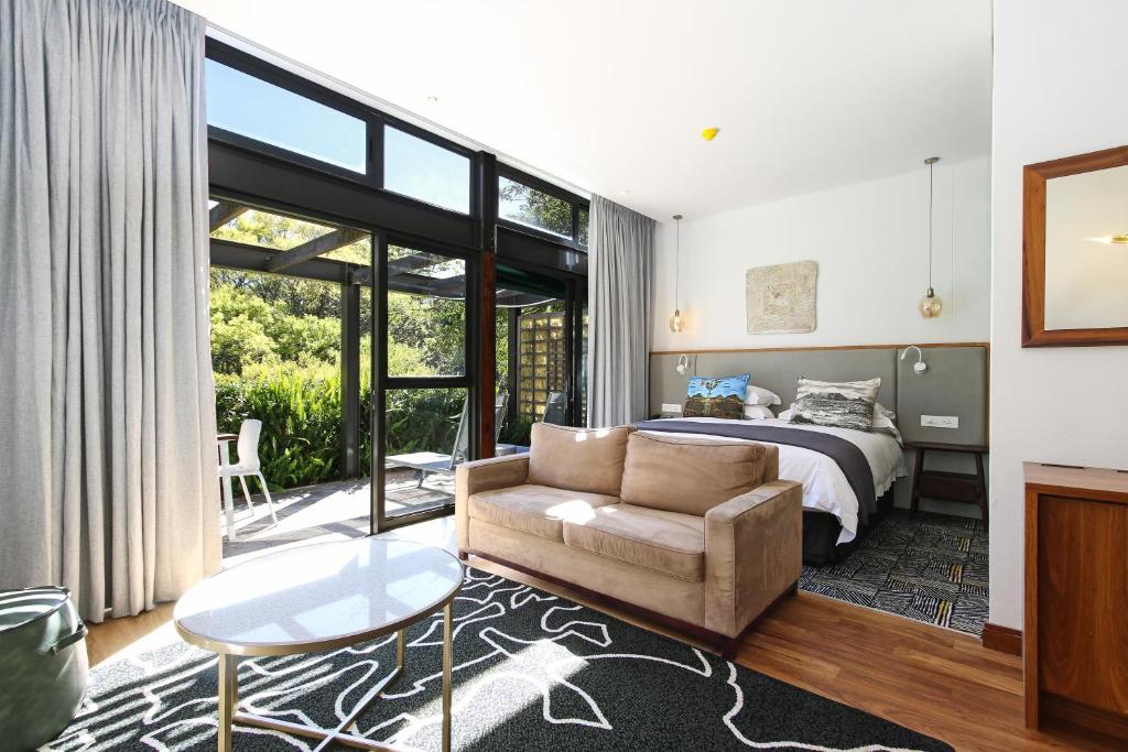 Hotel room with a king bed, tan sofa, and glass doors opening to an outdoor patio with greenery visible outside the suite.