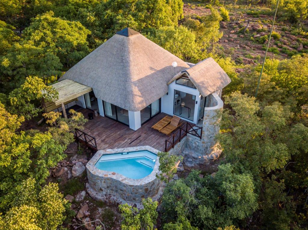 A thatched-roof villa on a wooden deck, surrounded by trees, with a stone-edged pool in the foreground.