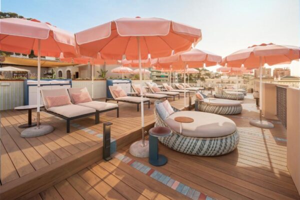 Rooftop lounge with pink umbrellas, cushioned daybeds, and wicker seating on a wooden deck.