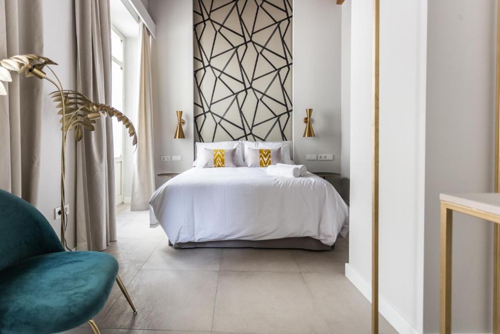 Modern hotel bedroom with a white bed, geometric black headboard, and gold bedside lamps in a bright room with a teal chair nearby.