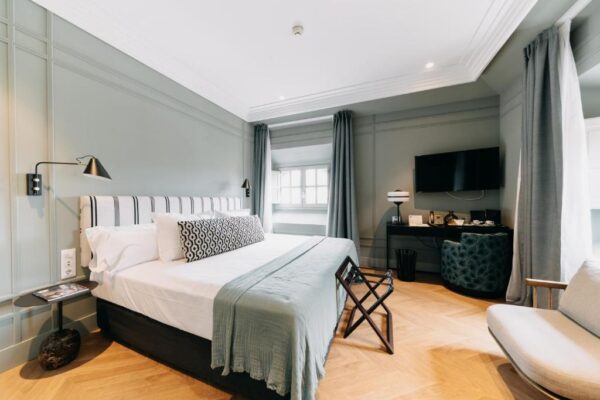 Cosy hotel room with a large bed, mint-green walls, and a seating area by a window.