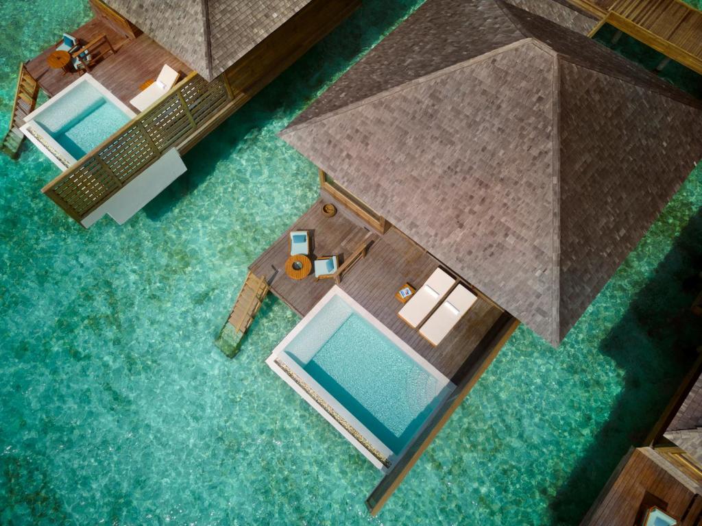 Aerial view of overwater bungalows with thatched roofs, wooden decks, and turquoise lagoon water.