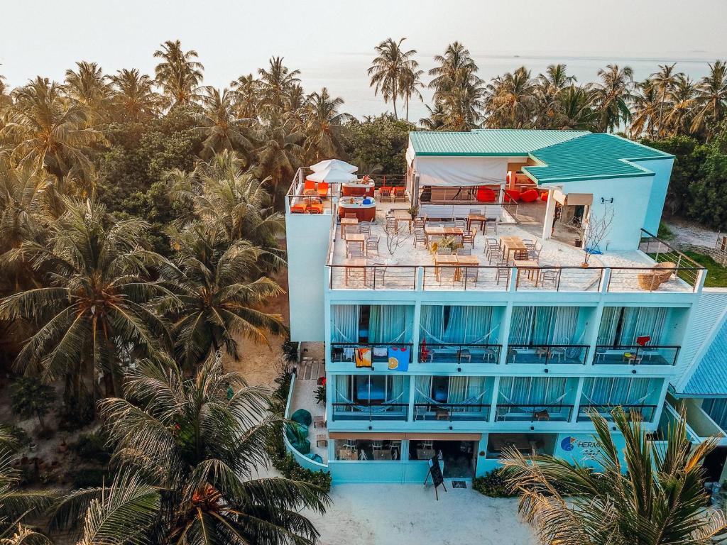 Aerial view of a turquoise, multi-story beachfront hotel surrounded by tropical palm trees.