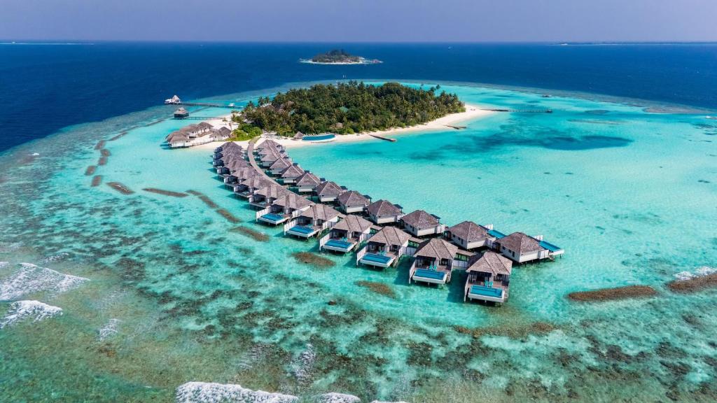 Aerial view of a tropical island resort with thatched overwater villas extending into a turquoise lagoon.”] ,