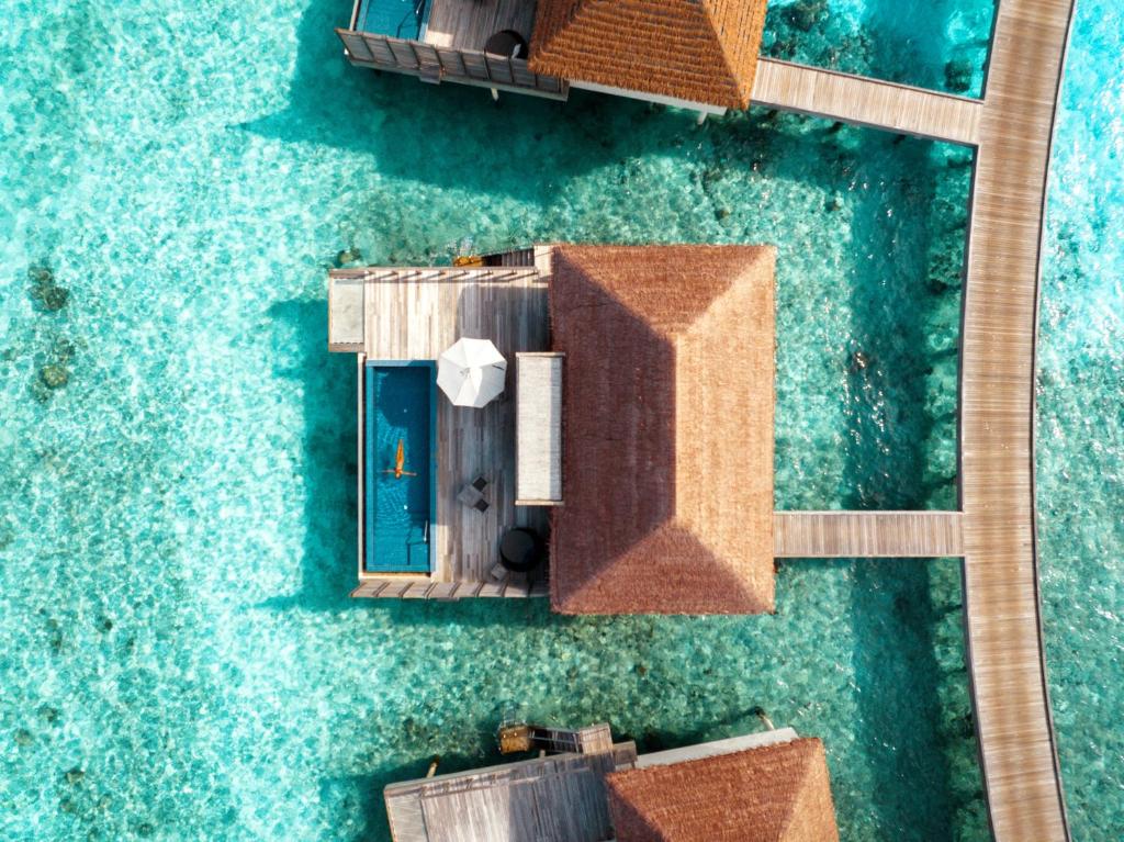 Aerial view of overwater bungalows connected by wooden walkways over clear turquoise water.