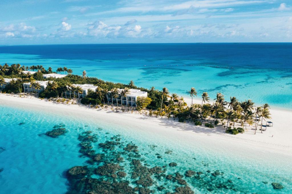 A tropical island with white sand beach, palm trees, and beachfront villas, surrounded by turquoise sea.