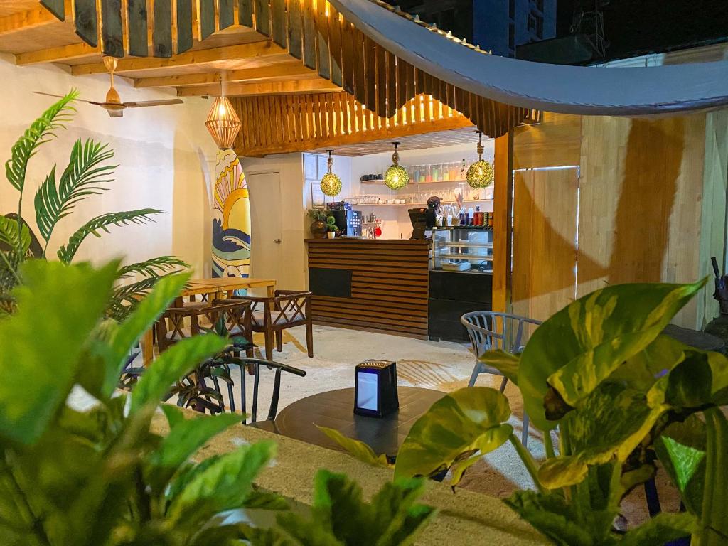 Cozy cafe interior with plants, wooden ceiling beams, round tables and chairs, and a counter with a barista under warm pendant lights.