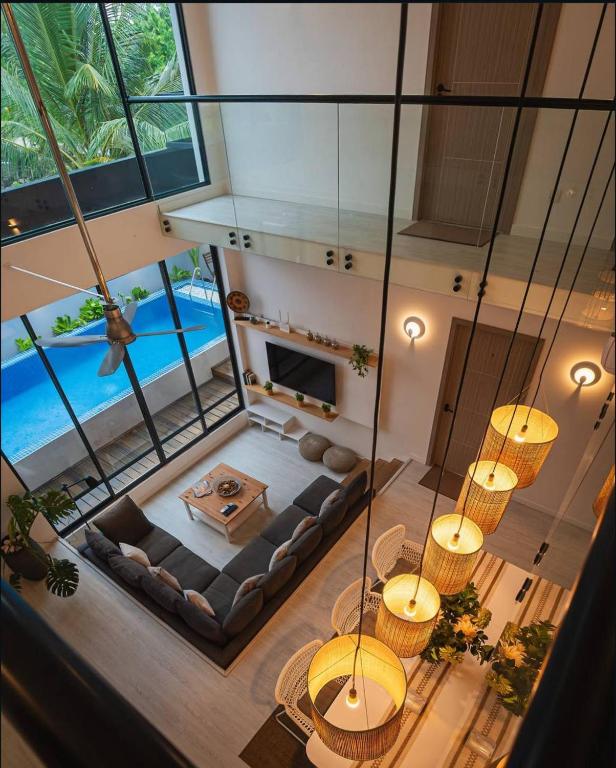 Open-plan living room with a U-shaped gray sofa, glass walls, and a view of the outdoor pool beyond. A coffee table sits on a rug facing a TV shelf.