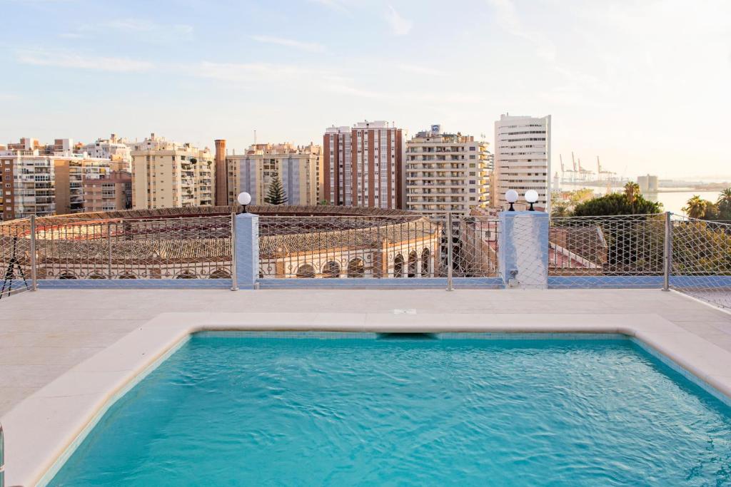 Rooftop swimming pool overlooking a city skyline with mid-rise buildings and a distant harbor on the right.