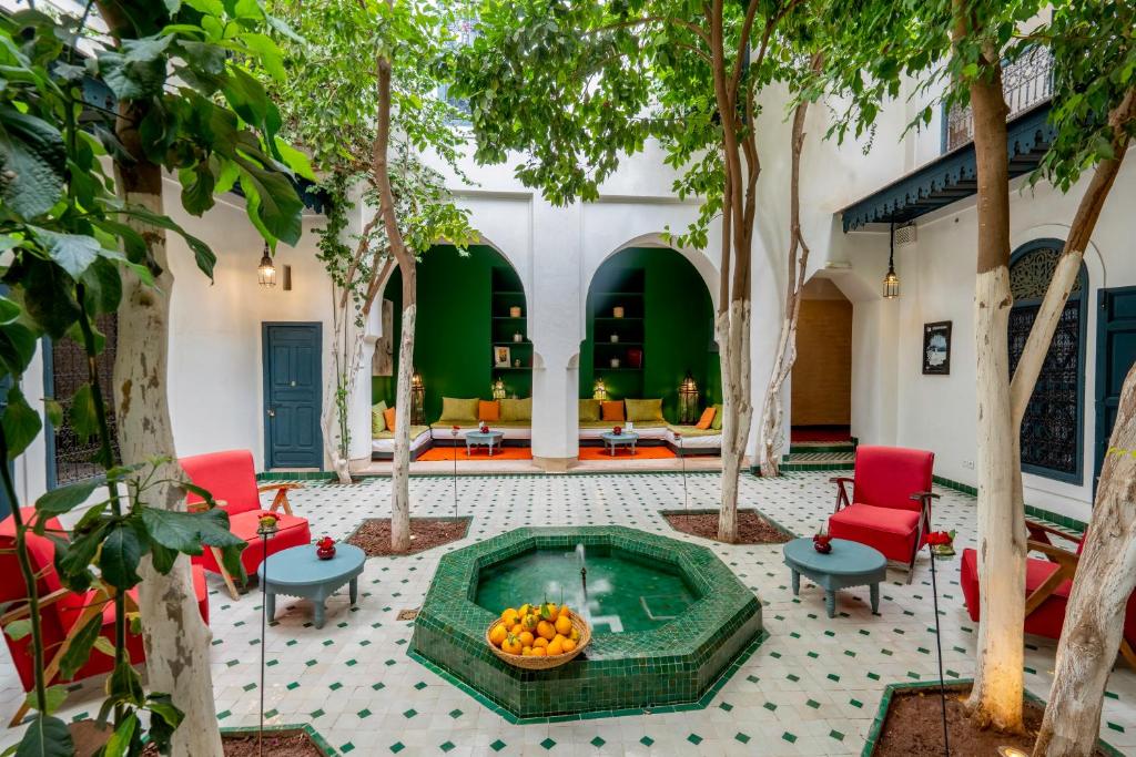 Courtyard with a central green tiled fountain, red chairs, and small gray tables under leafy trees.