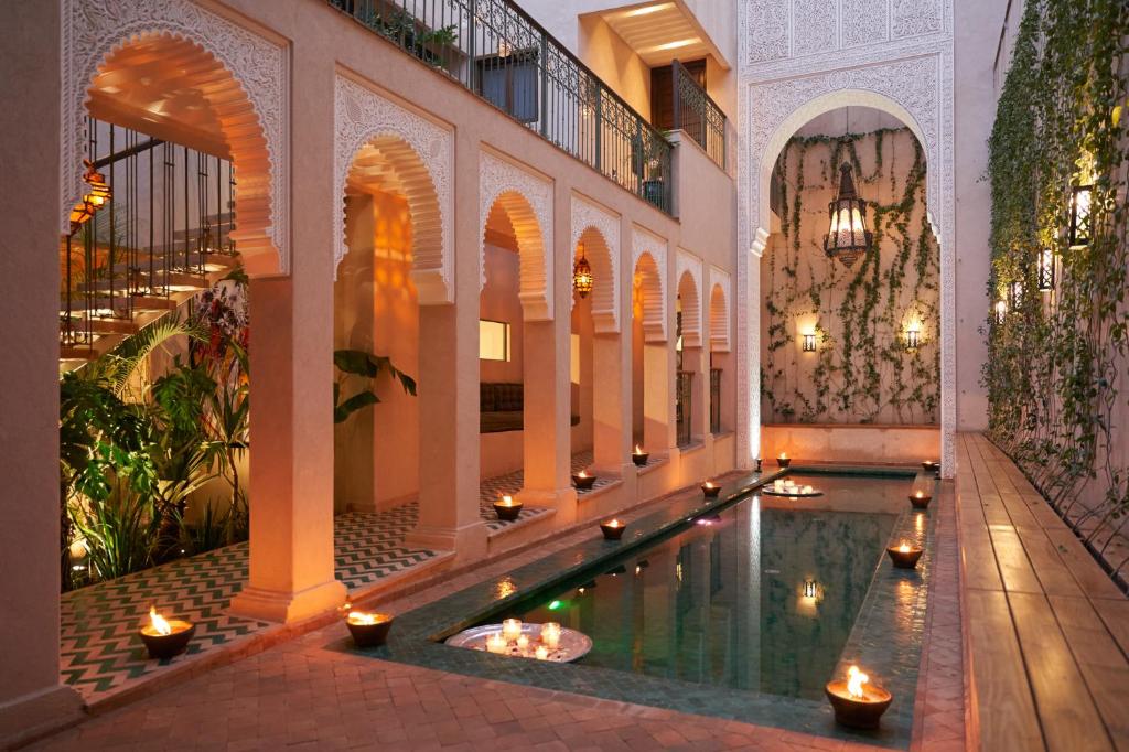 Indoor courtyard with white arches, a narrow reflective pool, and candles lining the edges.