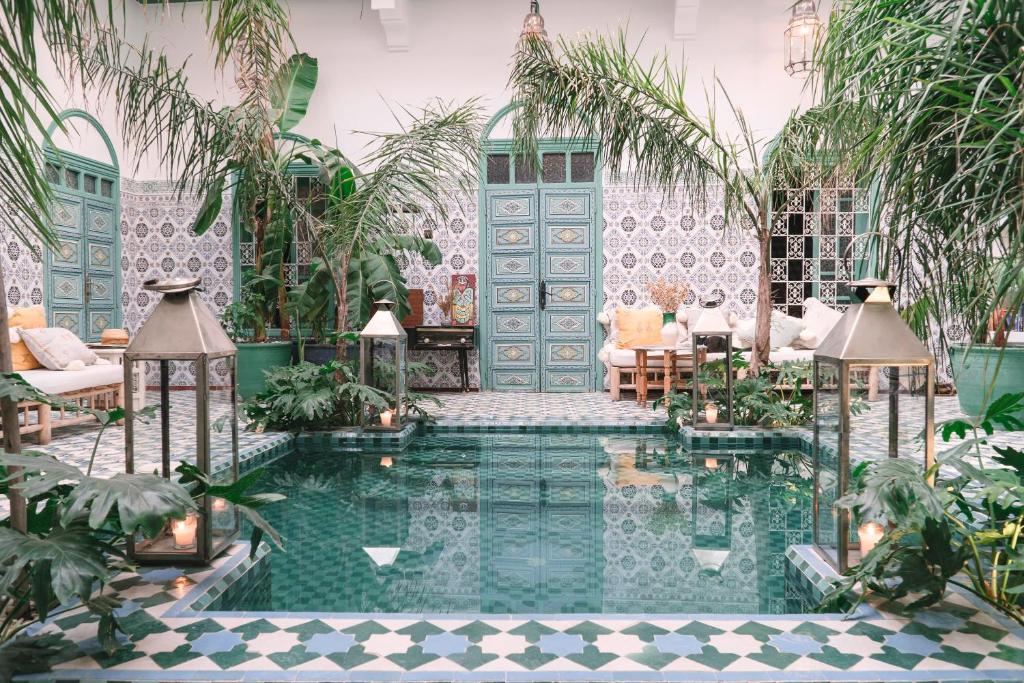 Indoor Moroccan-style courtyard with teal doors, lush plants, and a reflective pool lined with patterned tiles.