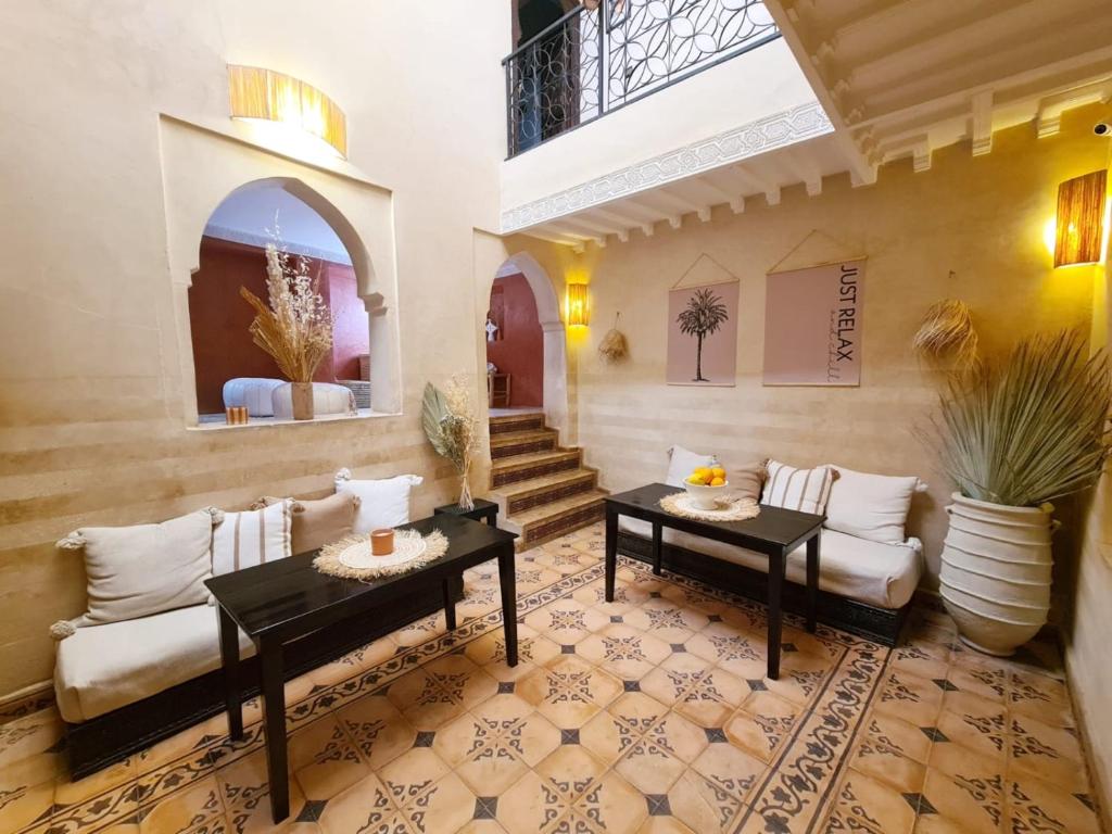 Indoor lounge with beige walls, two black coffee tables, white cushioned seating, and potted plants under warm lighting.