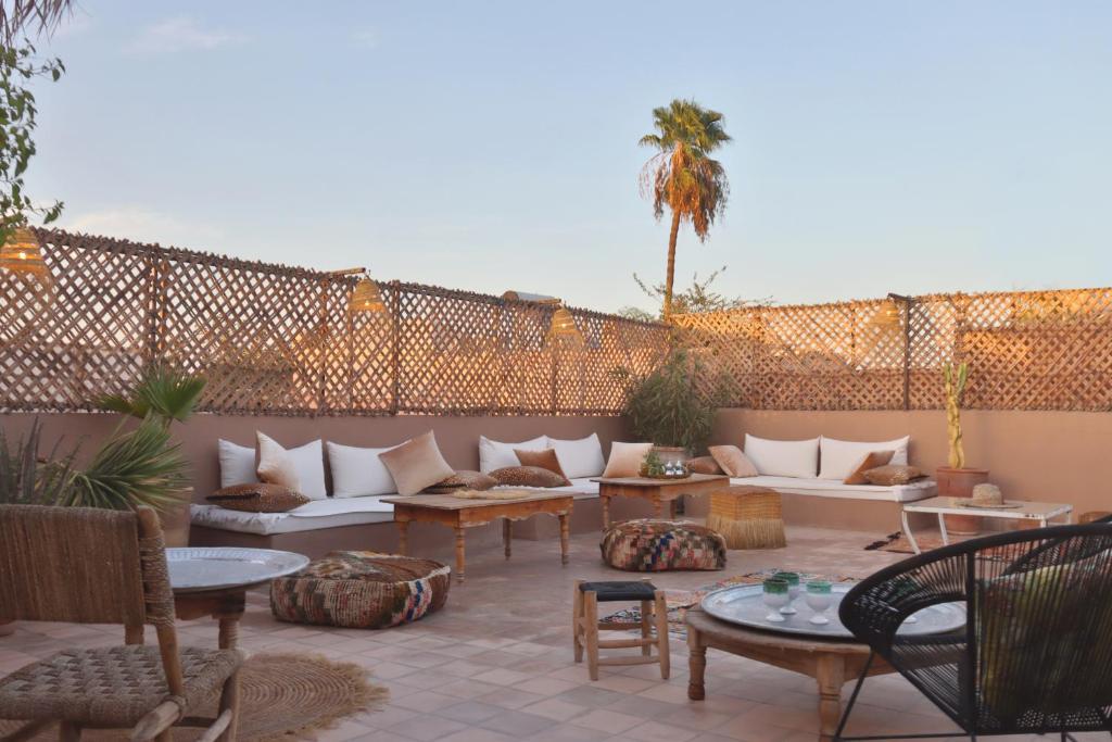 Outdoor lounge on a tiled patio with white-cushioned sectional seating, wicker chairs, and low wooden tables under a lattice privacy screen with a palm tree in the background.