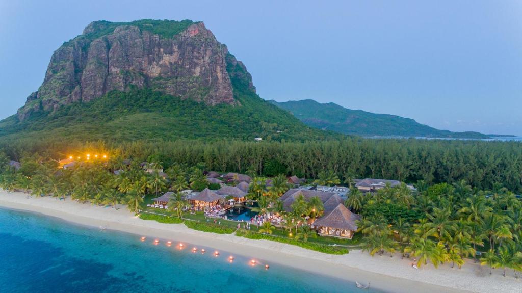 Tropical resort along a white-sand beach with palm trees, thatched cottages, and a forested mountain in the background.