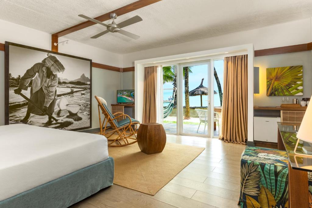 Hotel room with a large black-and-white wall art, front bed, and sliding glass doors to a beach scene with palm trees and a hammock outside.