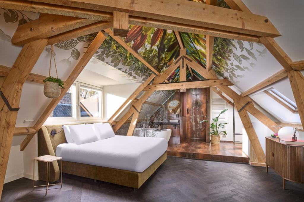 Rustic attic bedroom with exposed timber beams, a white bed, and a hanging plant, sunlit by skylights.