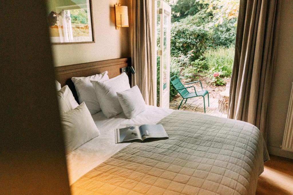 A cozy hotel bedroom with a large bed, white pillows, and an open magazine resting on a quilted cover, door open to a garden patio.