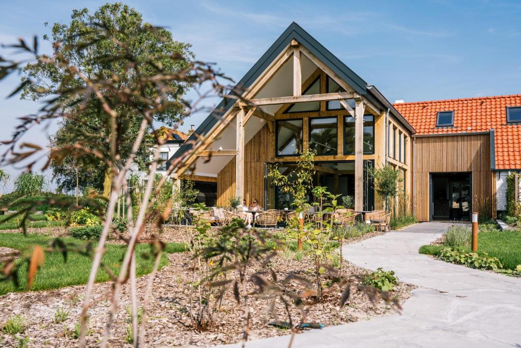 Modern wooden building with large glass windows and a timber frame, outdoor seating on the patio under clear blue skies.
