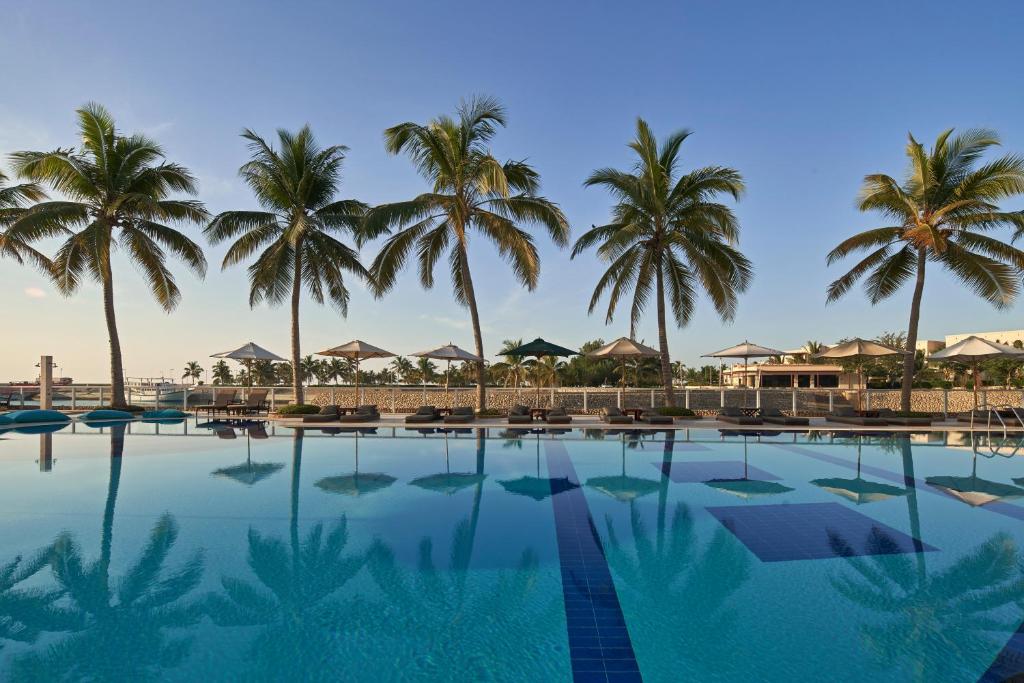Resort pool bordered by palm trees and lounge chairs under a clear blue sky.