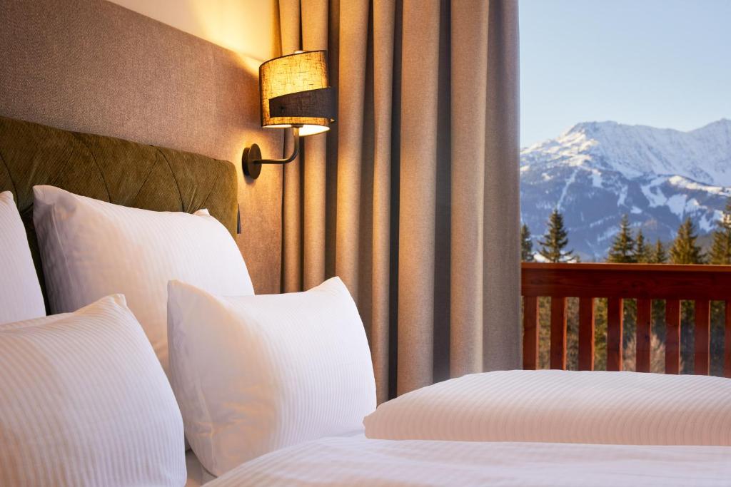 Hotel bed with white pillows and a warm wall lamp, beige curtains, and a balcony overlooking snowy mountains.