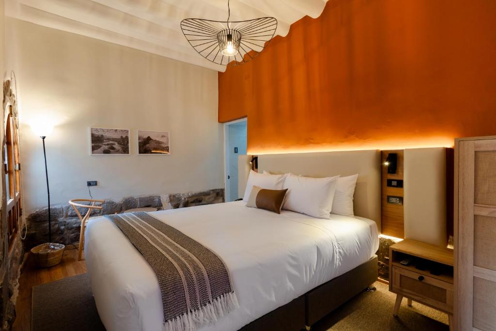 Hotel room with a large white bed, brown accent pillow, and orange accent wall with backlighting behind the headboard.