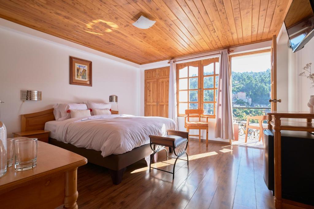 Bright hotel room with a large bed, white linens, and a balcony door letting in sunlight through wooden-framed windows.