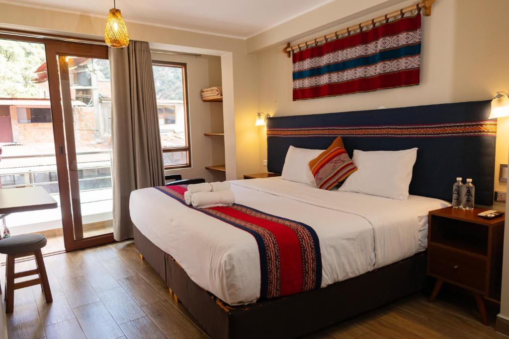 Hotel room with a king bed, navy headboard, white linens, and a colorful woven runner; balcony door to outside.