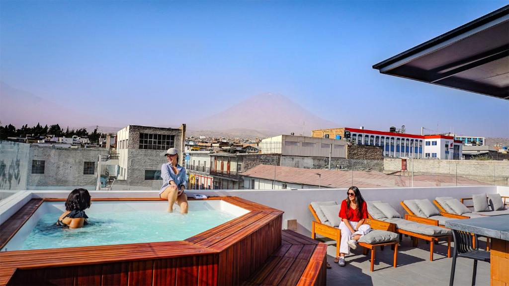 Rooftop pool with two women lounging, city buildings and a distant volcano in view.