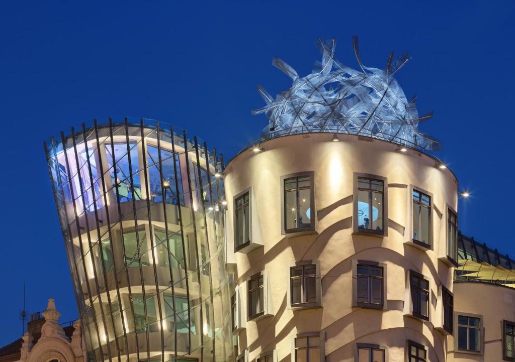 Evening view of La Pedrera (Casa Milà) in Barcelona with a rounded beige façade, numerous windows, and a sculptural metal rooftop installation.
