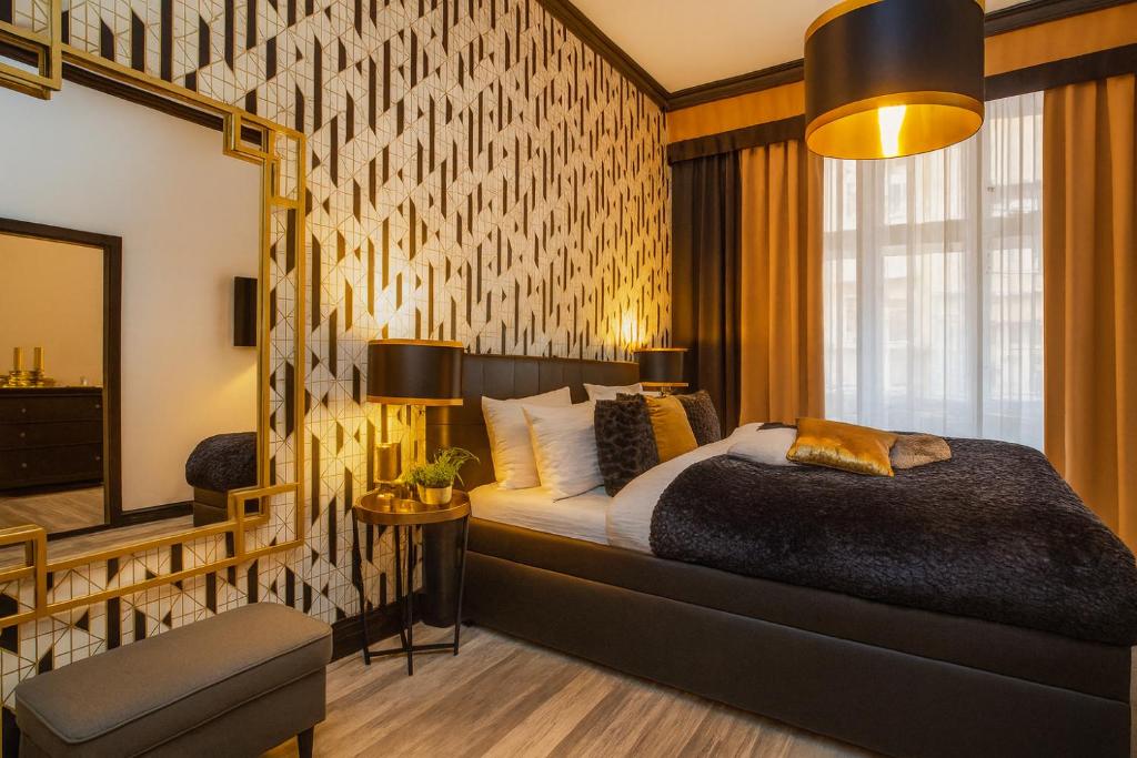 Luxurious hotel bedroom with a geometric patterned accent wall, a dark upholstered bed, gold bedside lamps, and beige curtains filter sunlight from a large window.