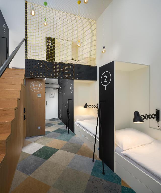 Modern hostel dorm area with private sleeping pods, numbered 2 and 4, white beds and black divider walls, colorful tiled carpet and hanging lights near a staircase.