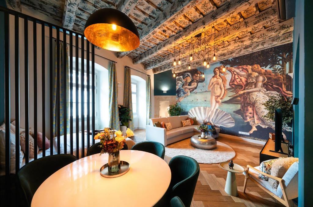Open-plan living and dining space featuring a mythological mural, beige sectional, and a round coffee table with a floral centerpiece.