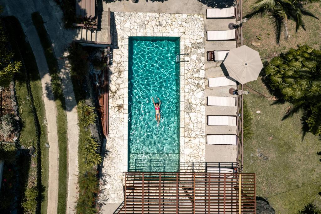 Aerial view of a rectangular pool with a stone deck, a swimmer in a pink swimsuit in the center, surrounded by lounge chairs and a large umbrella.