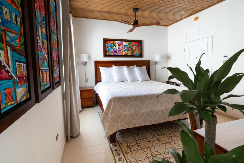 Hotel bedroom with king bed, white linens, wooden headboard, two nightstands, and colorful framed art above the bed, ceiling fan overhead.