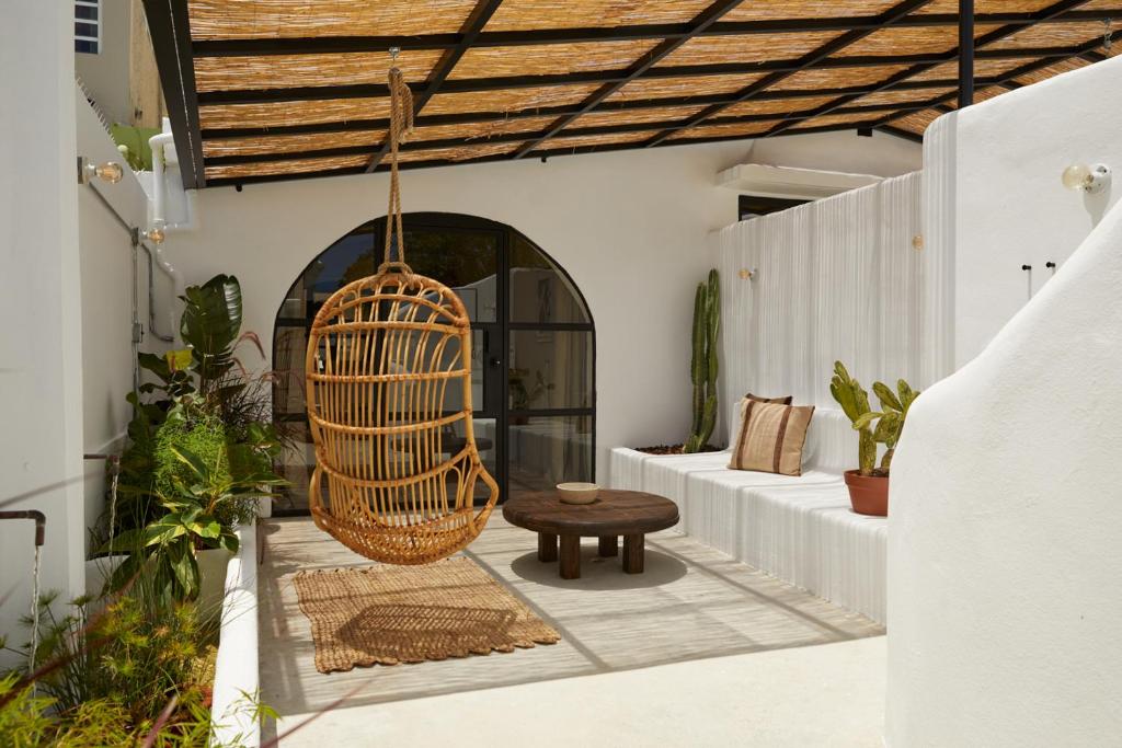Courtyard seating area with a hanging wicker chair, a round wooden coffee table, and potted plants along white walls under a woven roof.