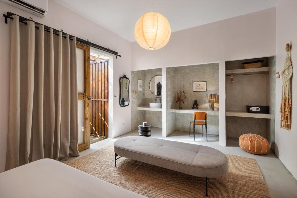 Minimalist bedroom with an oval gray bench on a woven rug, beige curtains, and built-in alcove desks.