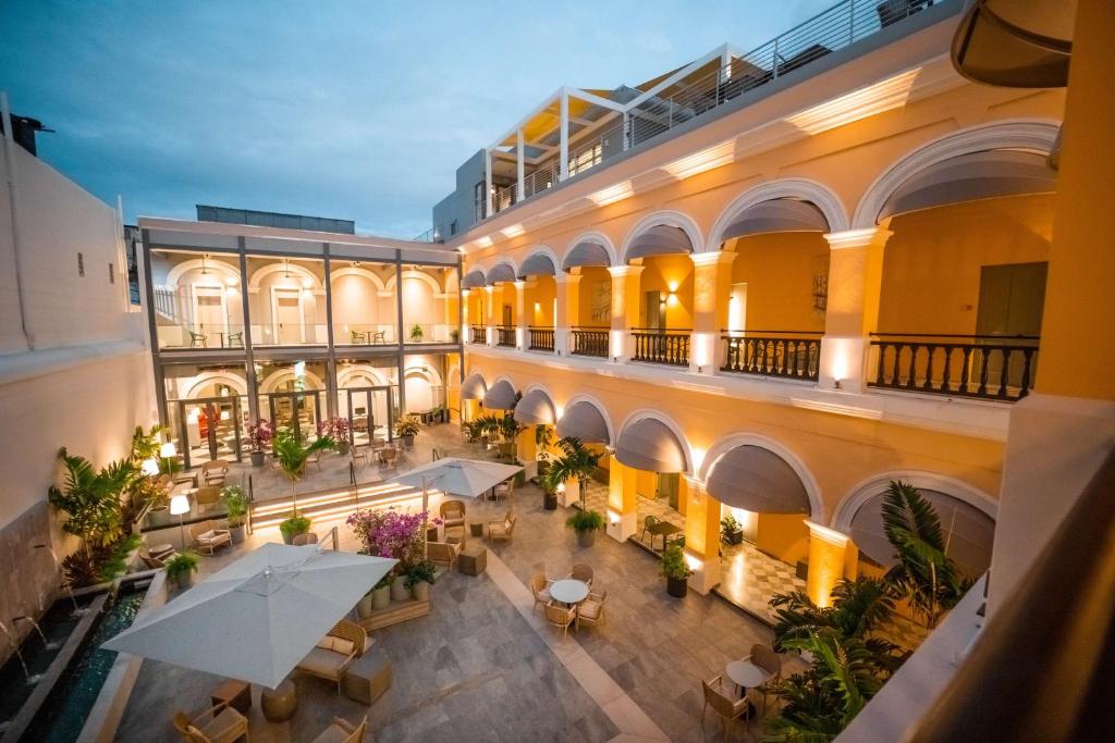 Twilight hotel courtyard with yellow arches, white arches, and warm lighting; outdoor seating under umbrellas for guests: lush plants nearby.