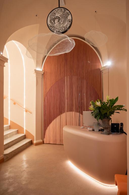 Reception desk with a curved beige counter and a large potted plant, fringed drapes behind a wooden arched wall, warm ambient lighting in a lobby.