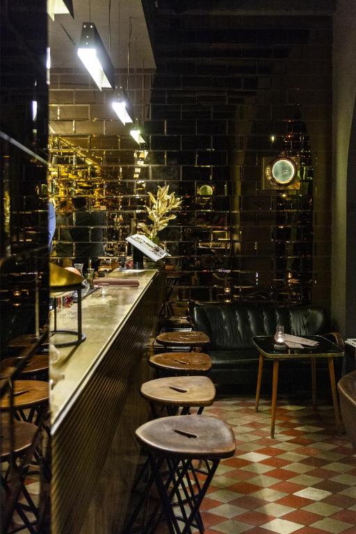 Dimly lit bar with a marble counter and a row of wooden stools along a glossy black tiled wall.