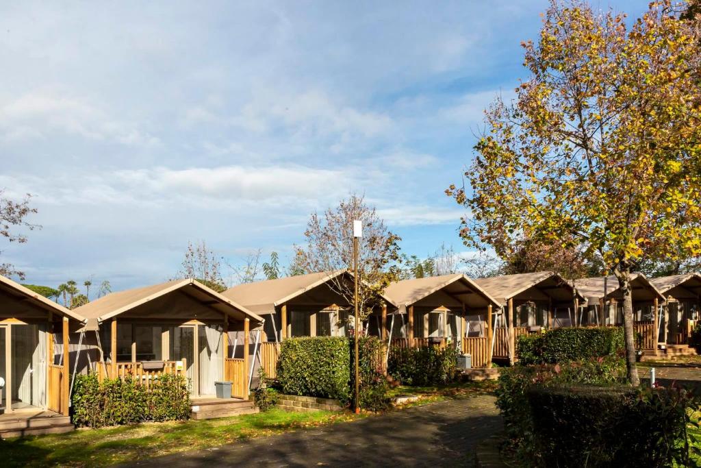 Row of beige canvas cabins with porches in a campground, autumn trees, and a clear blue sky.