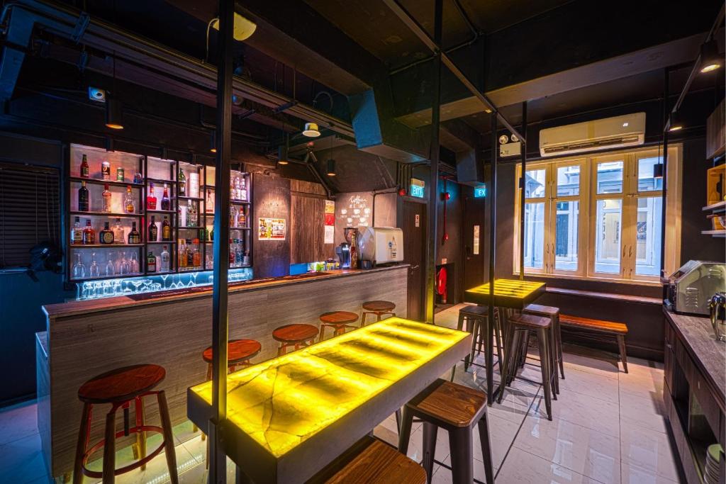 Contemporary bar with a glowing yellow-lit counter, wooden stools, and shelves of bottles behind the bar.