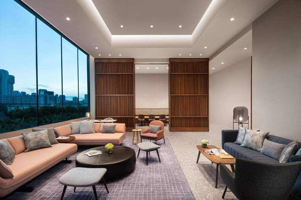 Spacious modern lounge with pink and blue sofas, low black coffee table, and floor-to-ceiling windows showing a cityscape.