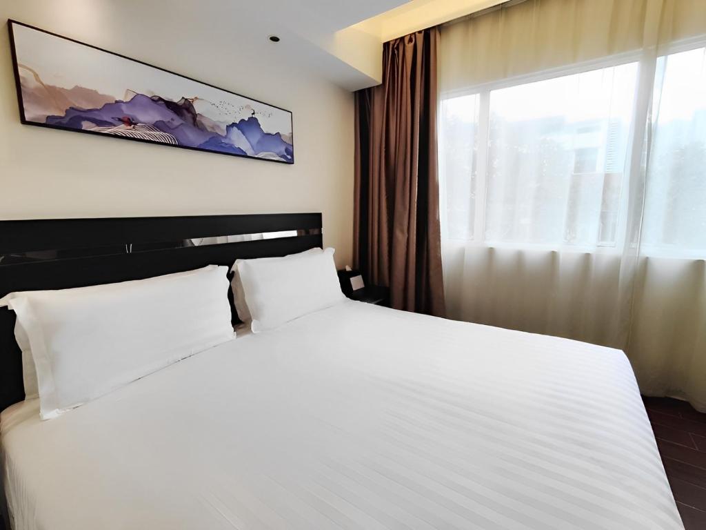 Hotel room with a large white bed, black headboard, and abstract wall art above. Neutral curtains by a sunny window.