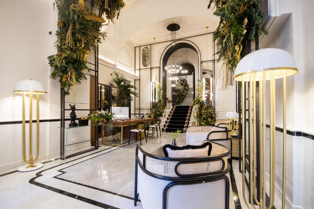 Luxurious hotel lobby with white marble floor, gold floor lamps, and lush greenery surrounding a central staircase.