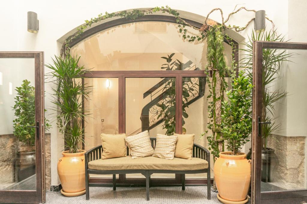 Cozy indoor seating area with a curved glass doorway, a spiral staircase in the background, and tall potted plants.