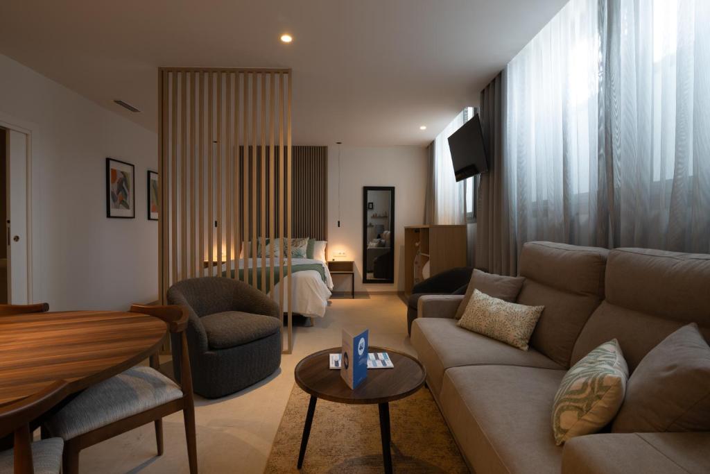 Hotel suite living area with a sofa, round coffee table, and a wooden slat divider separating the bedroom.