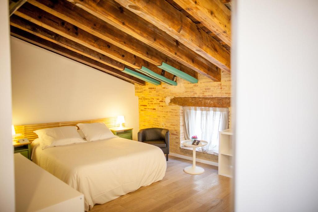 Attic bedroom with a white bed, green bedside tables, and warm lamps, exposed wooden ceiling beams, and a brick wall.