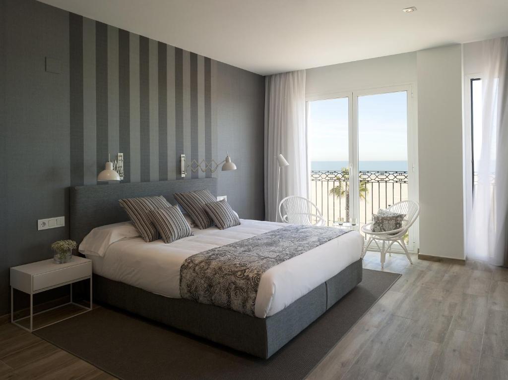 Modern hotel room with a king bed, gray upholstery, and a balcony with ocean view. Restful, striped wall backdrop enhances the space.